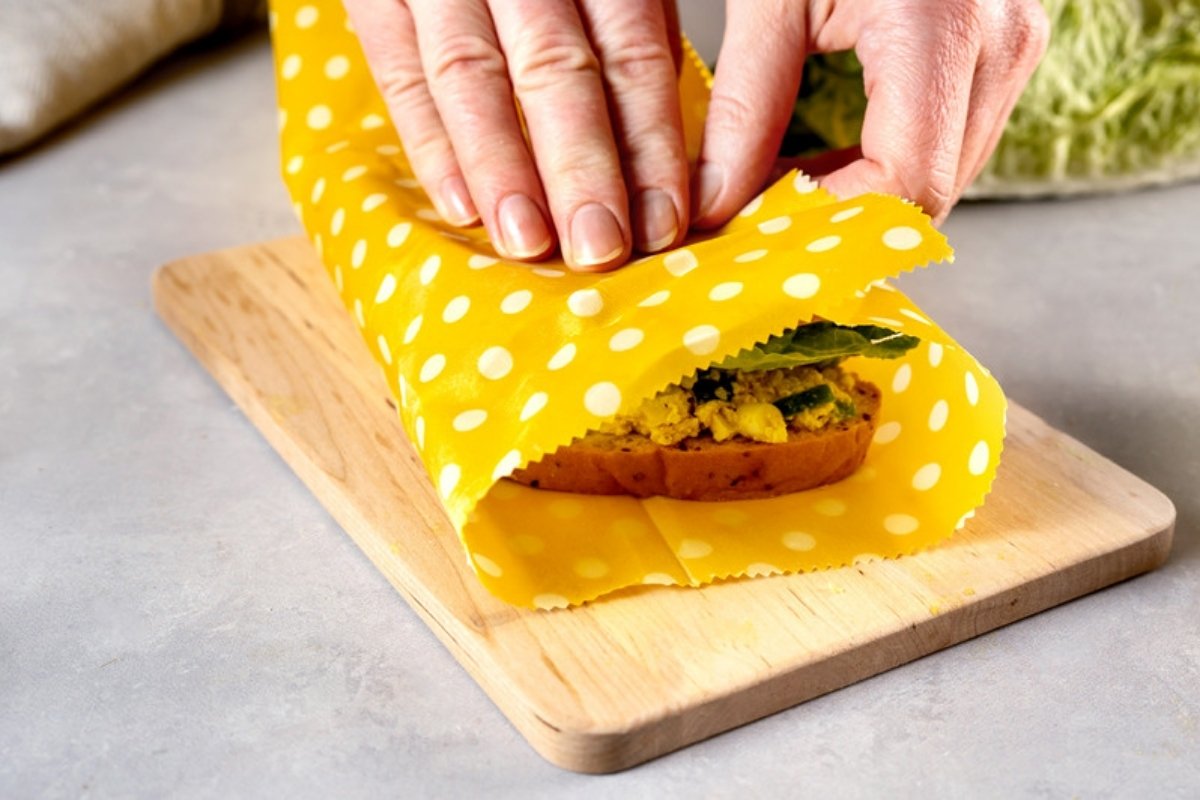 Hands wrapping a sandwich in a yellow polka dot beeswax food wrap
