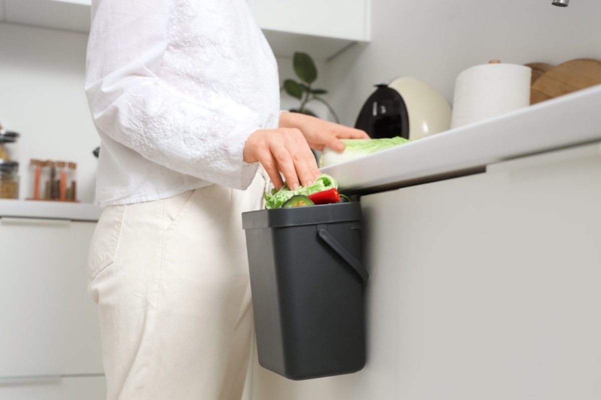 Woman putting vegetable scraps into a small kitchen compost bin