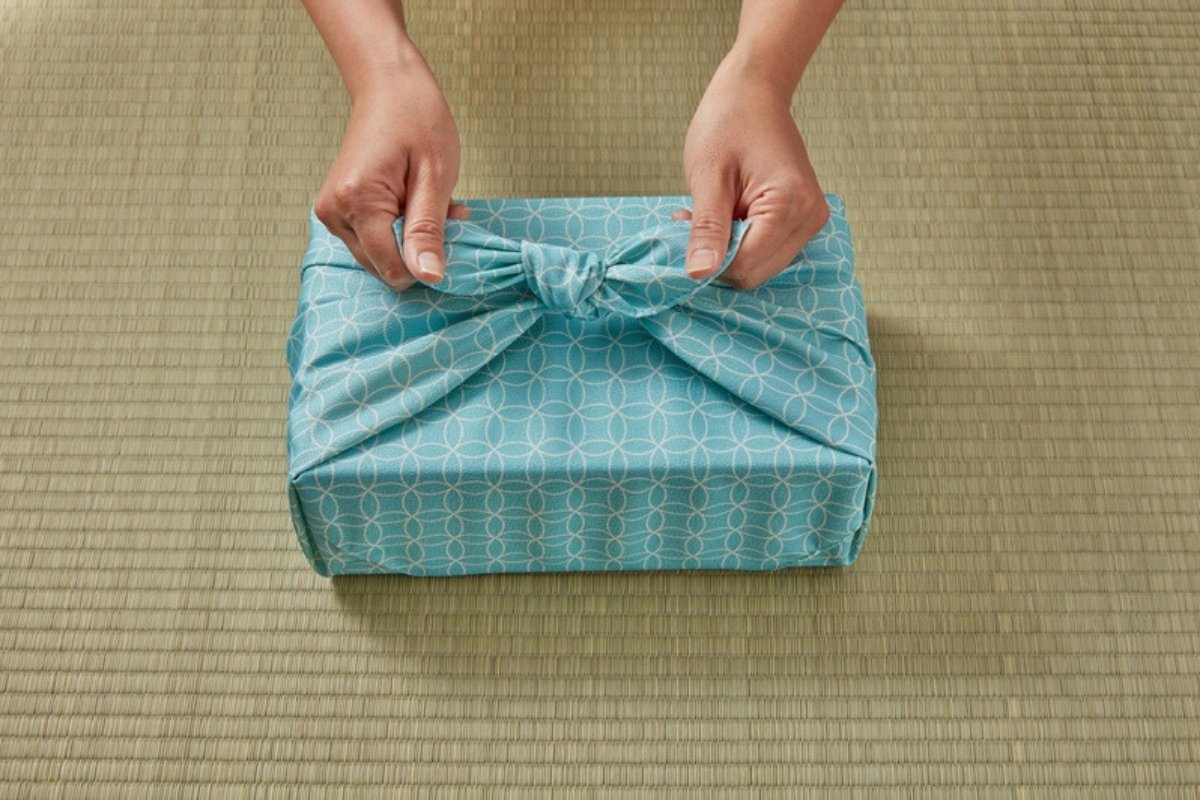 Hands tying a knot on a gift wrapped furoshiki style in blue patterned fabric