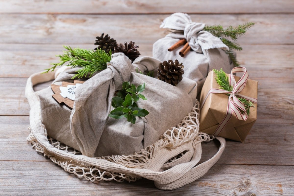 Fabric-wrapped Christmas gifts with pine and pine cones in a reusable cotton mesh bag